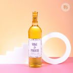 A bottle of wine with a customized label that reads 'Mike & Phoebe 2018', positioned on a surface with wine glasses and a circular yellow object in the background.